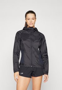 Svart lättviktsjacka med huva, dragkedjestängning, sidopaneler och en slät textur. Matchas med svarta shorts.
