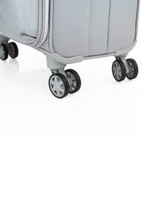 Maleta rígida gris con cuatro ruedas negras multidireccionales, textura de tela suave y una cremallera que recorre los bordes.