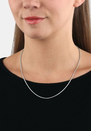 Collana in metallo color argento con un design liscio e flessibile. Ha una forma elegante e minimalista e si posiziona appena sotto la clavicola.