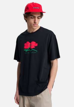Sort t-shirt med korte ærmer med et rødt blomsterprint med grønne accenter og teksten "Quiksilver" nedenunder. Bruges med en rød kasket.