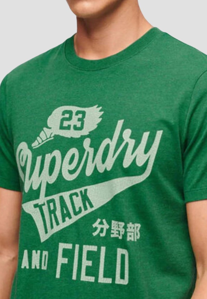 T-shirt in cotone verde con testo bianco che recita "Superdry Track and Field" e un grafico di una sneaker con il numero "23."