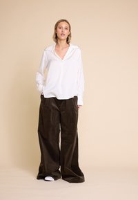 Hvit langermet bluse med V-hals og oversized brune kordfløyelsbukser, med vide ben og en myk tekstur.