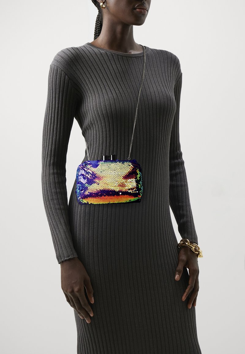 Clutch de lentejuelas multicolores con forma rectangular, hardware negro y cadena. Llevado sobre un vestido de punto acanalado gris texturizado.