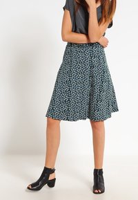 Hame tumman vihreästä kankaasta, jossa on vaaleansinisiä ja valkoisia kukkakuoseja. A-linjainen malli, keskipituinen, yhdistetty mustiin korkokenkiin.