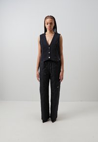 Černá denimová vesta s hlubokým výstřihem do V a předními knoflíky, spárovaná s černými prošívanými širokými kalhotami se strečovým pasem a bočním logem.