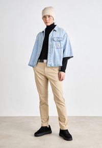 Ljust blå denim jacka med kort ärm och framficka; svart polotröja; beige byxor; svarta sneakers; beige basker med etikett.