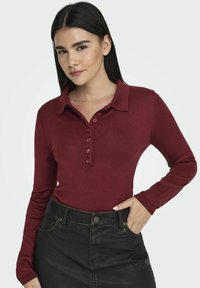 Bordeaux langekleurige poloshirt met een kraag, voorzien van een knoopsluiting en geribbelde textuur, gecombineerd met een zwarte hoge taille rok.