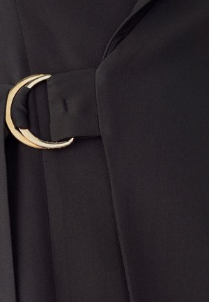 Schwarzer Stoff mit einem eleganten Design, versehen mit einer goldenen, runden Schnalle, die einen Gürtel akzentuiert. Die Textur ist glatt und maßgeschneidert.