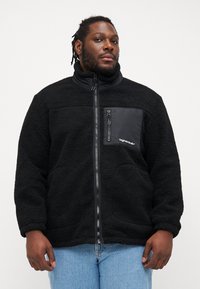 Μαύρη φλις ζακέτα με ψηλό γιακά, φερμουάρ μπροστά και τσέπη στο στήθος. Διαθέτει υφή υφάσματος και αντίθετο υλικό τσέπης μαύρου χρώματος.