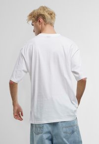 Hvid oversized t-shirt med korte ærmer, der har en klassisk rund halsudskæring. Stoffet ser blødt og glat ud, med en afslappet pasform.