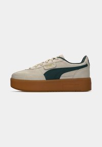 Low platform sneaker with beige suede upper, dark green Puma stripe, beige laces, and thick gum rubber sole.