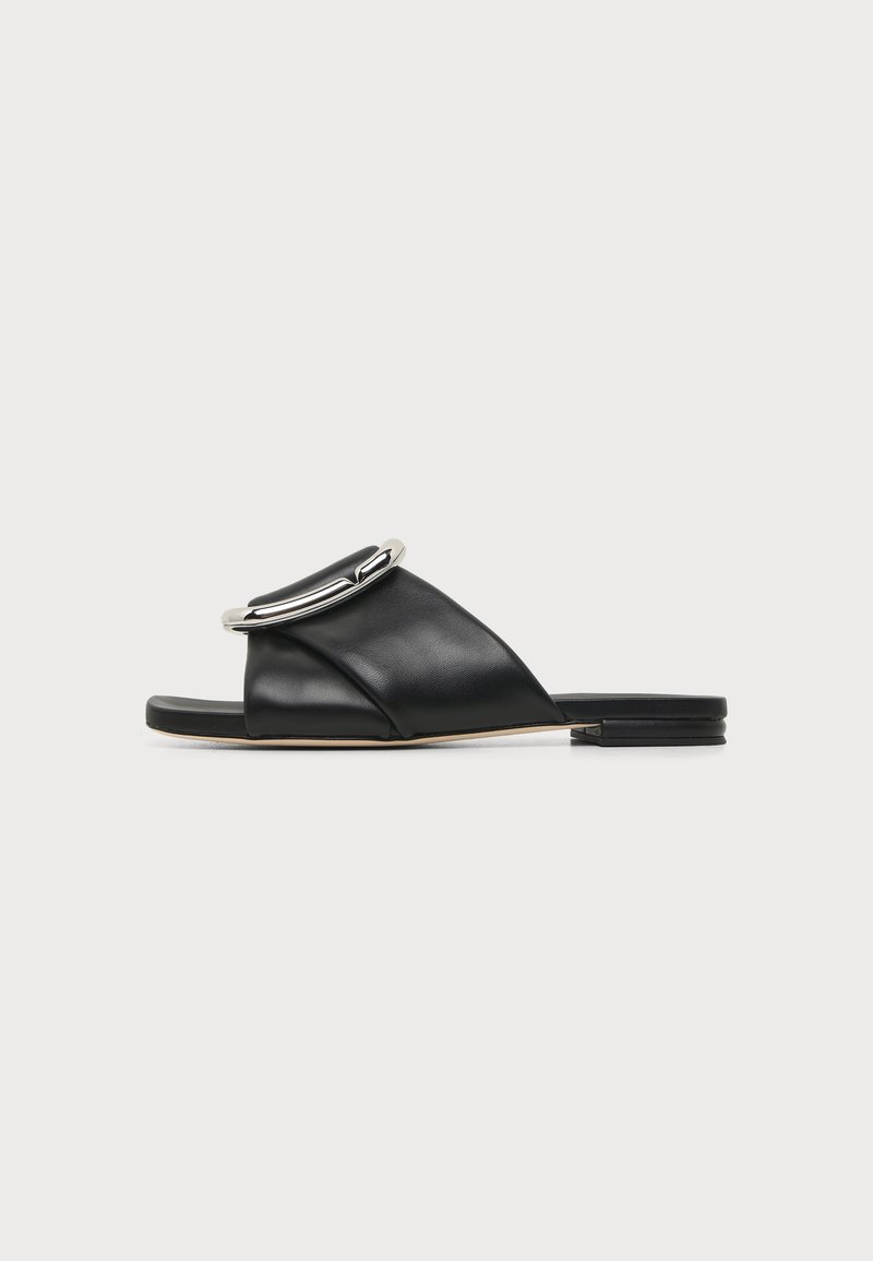 Sandale slide en cuir noir avec une large bride, une grande boucle argentée, une semelle plate et un petit talon empilé sur fond blanc.