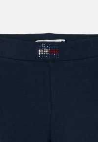 Marina blå leggings med en slät yta och ett brett midjeband, som har ett dekorativt mönster av rhinestones i röd, vit och blå.