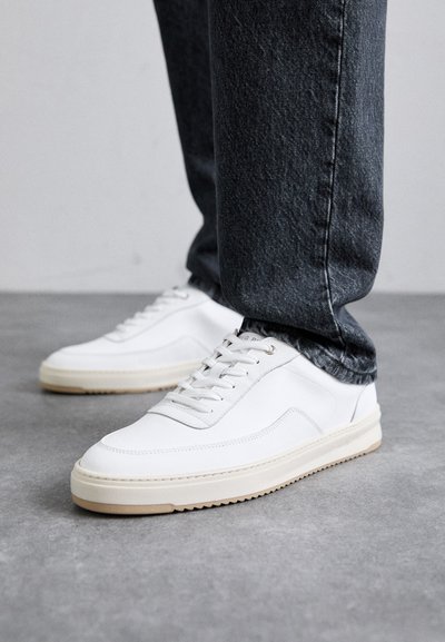 Hvite lærsko med teksturerte paneler, rund tå og kremfarget gummisåle. Kombinert med mørk denimjeans.