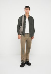 Mørkegrønn kordfløyels skjorte med knapper over en hvit singlet, kombinert med beige jeans og svarte chunky sko. Inkluderer grå skulderveske.