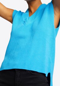 Blau gerippter ärmelloser Stricktop mit einem V-Ausschnitt, seitlichen Schlitzen und strukturiertem Stoff, kombiniert mit schwarzen Unterteilen.