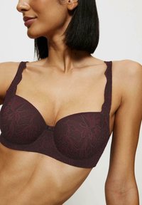 Bordowy koronkowy biustonosz z kwiatowym wzorem, wsparcie w postaci fiszbin, regulowane ramiączka i falbaniaste brzegi. Charakteryzuje się gładką fakturą i usztywnionymi miseczkami.