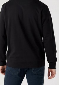 Svart sweatshirt med rund halsringning, långa ärmar och ribbade muddar, kombinerad med blå jeans, vilket ger en avslappnad och bekväm passform.