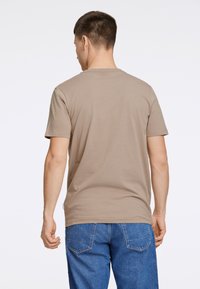 Beige t-shirt med kort ärm i mjukt tyg, med rundad halsringning och en avslappnad passform, kombinerat med blå jeans.