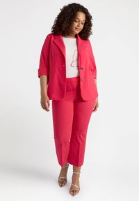 Röd skräddarsydd kavaj och matchande korta byxor med små silverförzieringar, kombinerat med en vit topp med röda detaljer.