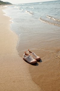 Heledalt roosad veejalatsid, millel on tekstuuriga kummist tald, elastsed avad ja väikesed dekoratiivsed mustrid, asetatud märjale liivale ookeani ääres.