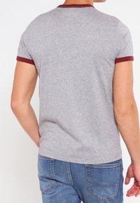 Grå t-shirt med kort ärm och vinröd kant vid hals och ärmar. Mjuk textur; figurnära design. Bärs tillsammans med blå jeans.