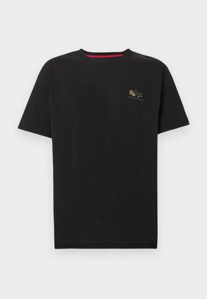 T-shirt noir à manches courtes et col rond avec petit logo Alpha Industries doré sur le côté gauche de la poitrine et détail rouge à l'intérieur du col.