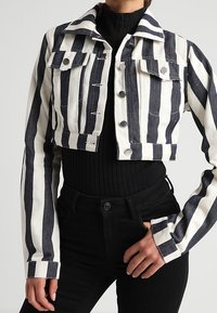 Kort jacka i marinblått och vitt randigt denimtyg, två bröstfickor, silverfärgade tryckknappar och krage. Styla med en svart topp.