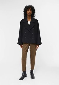 Sort dobbeltradet jakke med store revers, kombineret med brune ternede bukser og sorte ankelstøvler. Ren design og skræddersyet pasform.