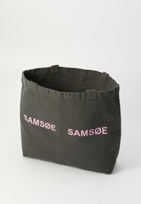Canvas tote bag i mørkegrå med dobbel "SAMSØE" trykt i rosa. Har korte håndtak og en strukturert, rektangulær form. Ingen lukking.