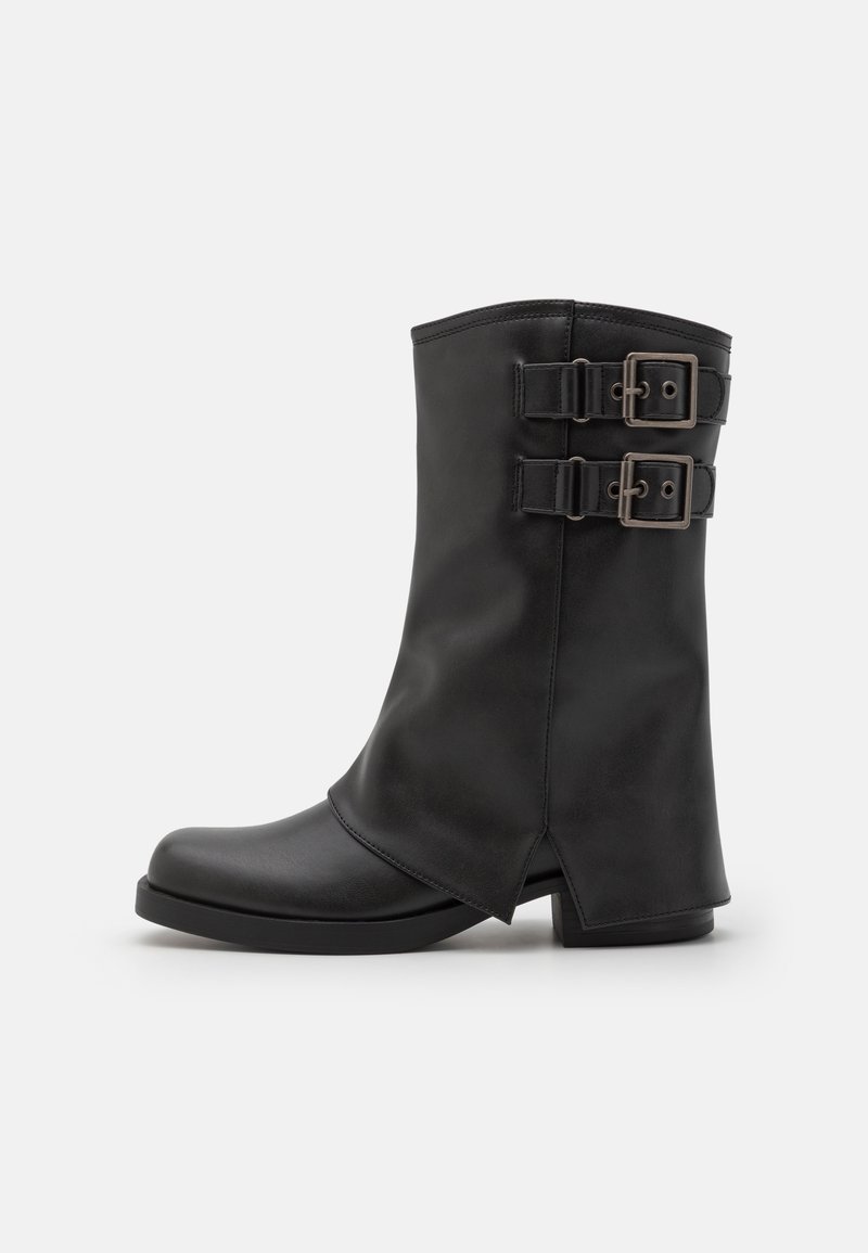 Botte noire en cuir mi-mollet avec deux sangles ajustables et boucles métalliques, semelle plate, et coupe en angle au talon et sur le panneau avant.