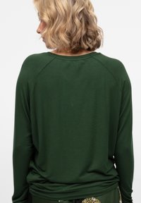 Camicia verde a maniche lunghe con texture a coste, maniche raglan e vestibilità rilassata, indossata da un modello visto di spalle.