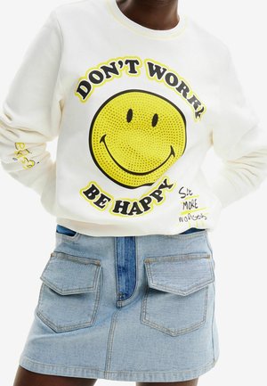 Bluza z dużą żółtą buźką i napisem „DON'T WORRY BE HAPPY” zestawiona z jasnoniebieską dżinsową spódnicą z frontowymi kieszeniami.