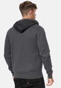 Haut à capuche gris foncé avec une capuche noire contrastante, tissu texturé, poignets et taille côtelés, et un logo discret à l'ourlet.