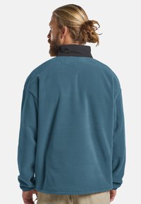 Fleece pullover in het blauw met een zwarte kraag. Heeft een ontspannen pasvorm, lange mouwen en een zachte textuur. De achterkant toont minimale naden.