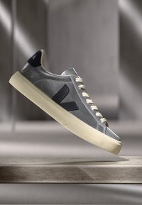 Sneakers in pelle grigia con finitura testurizzata, dettagli in blu navy, suola in gomma avorio e lacci beige chiaro, con un logo prominente sul lato.