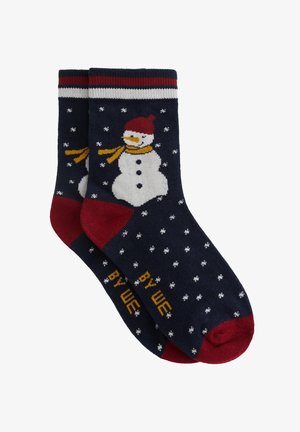 Chaussettes navy avec un motif de bonhomme de neige, des accents rouges, des flocons de neige blancs et une écharpe jaune. Haut côtelé avec des détails de logo en jaune.