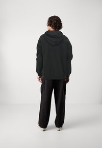 Black hoodie with a large hood, relaxed fit, and ribbed cuffs. Paired with loose, dark cargo pants featuring side pockets.