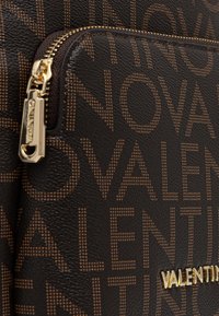 Zwarte leren tas met textuur, voorzien van een lineair bruine letterpatroon, gouden ritshardware en een opvallend gouden "VALENTINO" logo aan de onderkant.