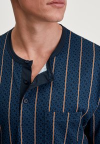 Camicetta blu navy a maniche corte con colletto a bottoni, caratterizzata da strisce verticali e un motivo geometrico, dotata di una tasca sul petto.