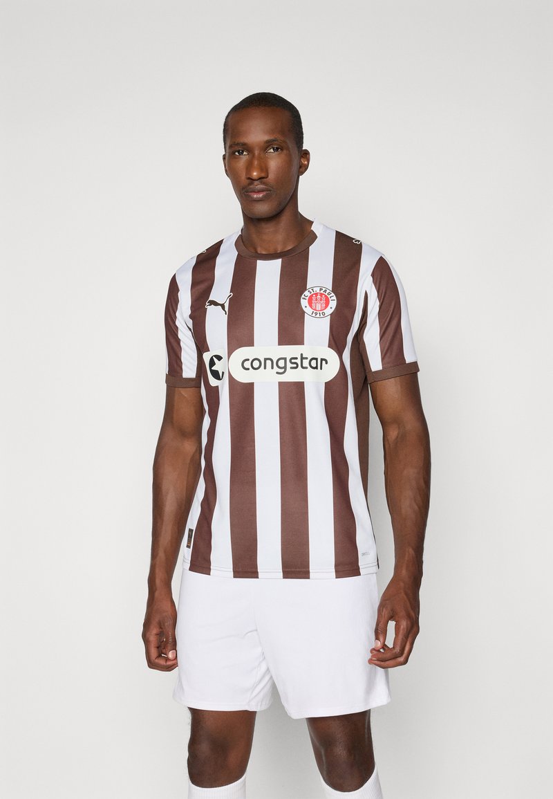 Brun og hvid lodret stribet fodboldtrøje med rund halsudskæring og brandlogo. Bæres med hvide shorts, der har et sponsorlogo.