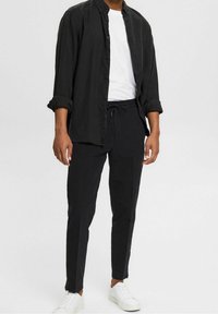 Czarna koszula na guziki z podwiniętymi rękawami, noszona na białej koszulce. Połączona z czarnymi spodniami na sznurku i białymi trampkami.