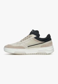 Beige sneaker met suède en leren panelen, zwarte accenten, ronde neus, zachte kraag en witte rubberen zool met een gestructureerd profiel.