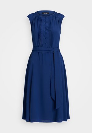 Vestido sin mangas de color azul marino con un bodice plisado, detalles de botones en la parte delantera, bolsillos laterales y un cinturón anudado en la cintura para mayor definición.