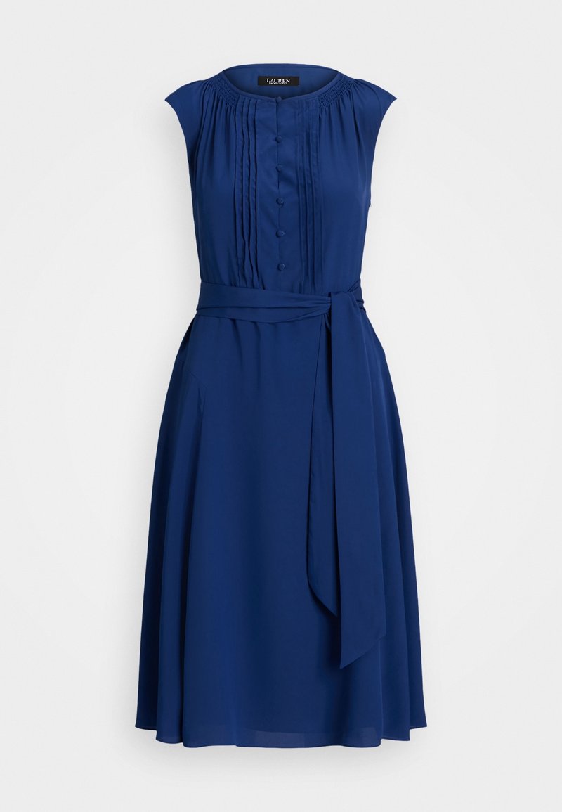 Vestido sin mangas de color azul marino con un bodice plisado, detalles de botones en la parte delantera, bolsillos laterales y un cinturón anudado en la cintura para mayor definición.