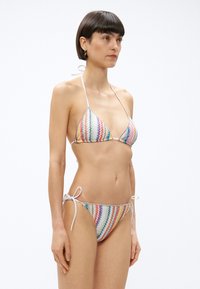 Bikini de patrón de chevron multicolor con top triangular y braguitas con lazos a los lados, hecho de tela suave con detalles brillantes.
