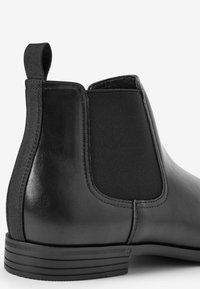 Svart läder Chelsea-boots med elastiska sidopaneler, slät textur, rund tå och en ribbad gummisula för bra grepp.