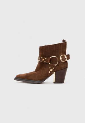 Bottes chelsea en daim marron avec un embout carré, boucle en métal doré et accents en métal, et une tige texturée. Présentent un talon empilé.
