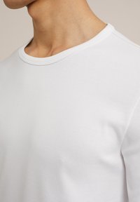Camiseta de algodón blanca de cuello redondo con una textura suave. Presenta un cuello acanalado y mangas cortas, destacando un diseño minimalista.