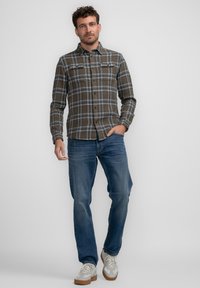 Geruit shirt in bruin en grijze tinten met lange mouwen en twee borstzakken, gecombineerd met blauwe jeans en beige sneakers.